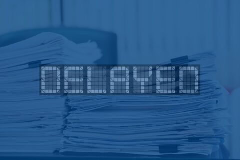 paper work piled high on a desk with the word delayed over it